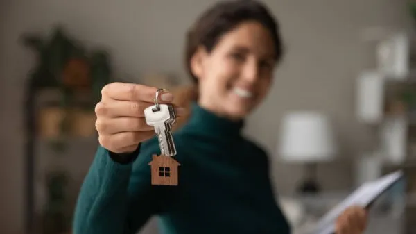 Imagen en donde se ve a una mujer que pertenece a una inmobiliaria y que se encuentra sosteniendo las llaves de una casa.